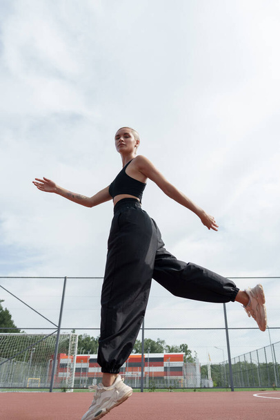 Eine überschwängliche Sportlerin springt mit offenen Armen vor blauem Himmel und zeigt Freiheit, Fitness und Freude an der Bewegung. - Foto, Bild