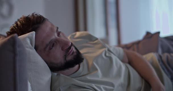 Deprimido barbudo adulto macho em roupas casuais deitado no sofá assistindo TV na sala de estar em casa - Filmagem, Vídeo