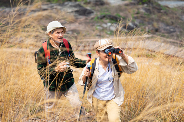 active asian senior couple hiking together on summer time,a female looking into binoculars and smiling,concept of elderly pensioner lifestyle,family relationship,activity,travel,adventure in nature - Photo, Image