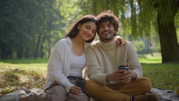 Šťastný usměvavý multietnický pár v lásce africký americký indián muž žena s piknik na dece park venku přítel přítelkyně kluk dívka těšit kávu romantické rande spolu objetí pózování v přírodě - Záběry, video