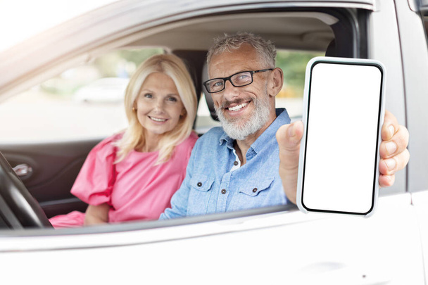Senior-Paar im Auto hält ein unbeschriebenes Smartphone mit digitalem Gerät, ideal für die Nutzung der Technologie unter Rentnern - Foto, Bild
