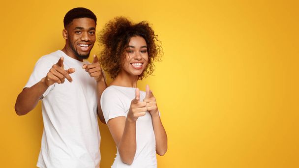 Gotcha Cheerful young african-american man and woman pointing fingers at camera, orange studio background - Photo, Image