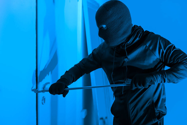 Вор, пытающийся взломать дверь ломом ночью, представляет собой типичный сценарий взлома, представляющий угрозу для безопасности квартиры. - Фото, изображение