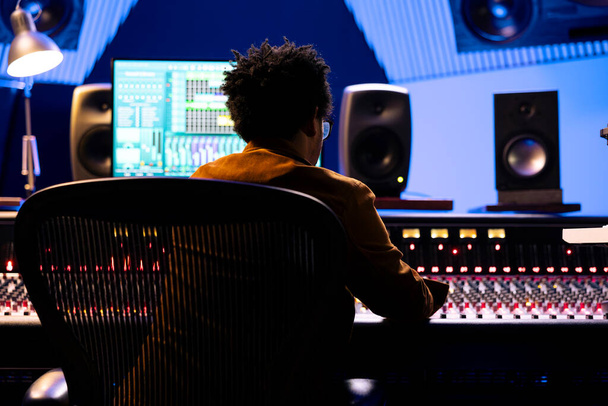 African American Record Engineer édite et mixe des chansons sur console studio, en utilisant un logiciel numérique sur moniteur pour ajouter des effets audio en post-production. Producteur travaillant sur de la nouvelle musique. - Photo, image