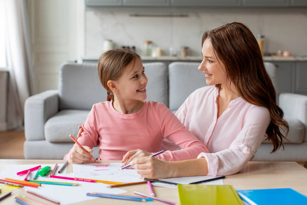 This image showcases a heartwarming European family scene of a mother and daughter sharing love and affection through drawing together at home - Photo, Image