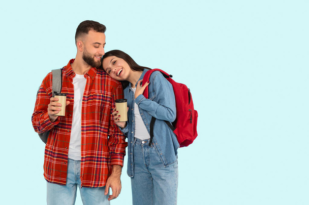 Nesta imagem, um jovem casal afetuoso, parte da geração z, está segurando xícaras de café e desfrutando de um momento juntos, isolados em um fundo azul. - Foto, Imagem