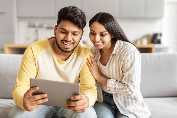 陽気な若いインドのカップルは,タブレット,おそらくオンラインで閲覧やショッピング,トータルネスとデジタルインタラクションを展示しています - 写真・画像