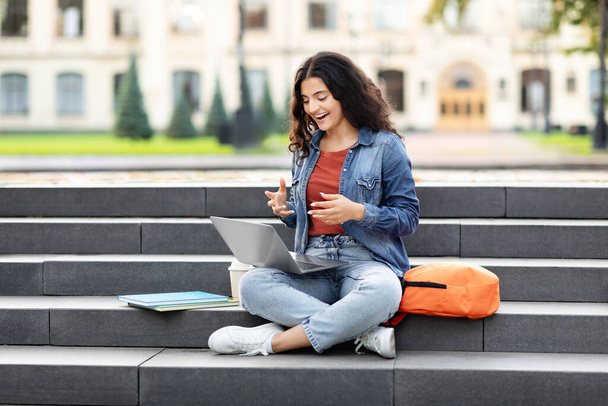 Egy fókuszált keleti nő lefoglalja a laptopját, ül a lépcsőn egy campus - a környezet a modern oktatás - Fotó, kép