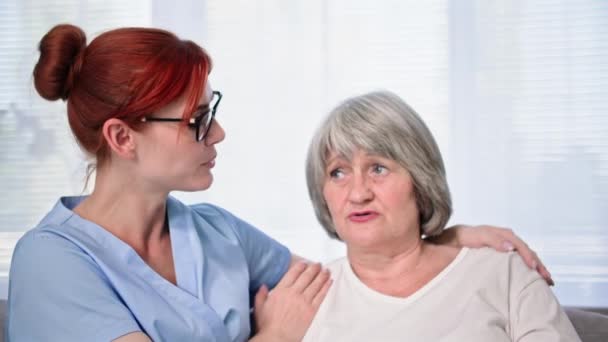 prendre soin des personnes âgées, jeune travailleuse sociale en uniforme médical fournit un soutien psychologique à la vieille femme tout en communiquant dans la chambre - Séquence, vidéo