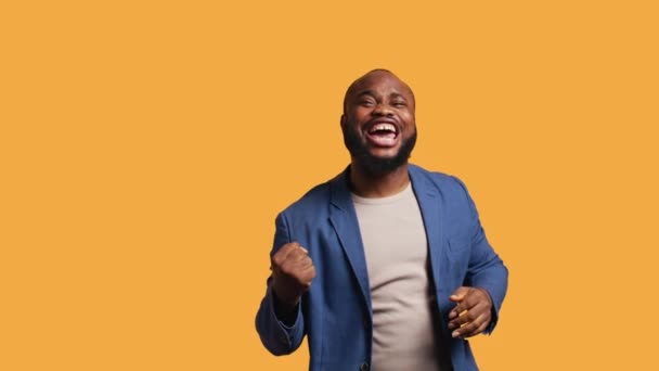 Porträt eines fröhlich fröhlichen afrikanisch-amerikanischen Mannes, der feiert und positive Emotionen zeigt. Entzückte BIPOC-Person begeistert von Leistung, Jubel und Gestik, Studiohintergrund, Kamera B - Filmmaterial, Video