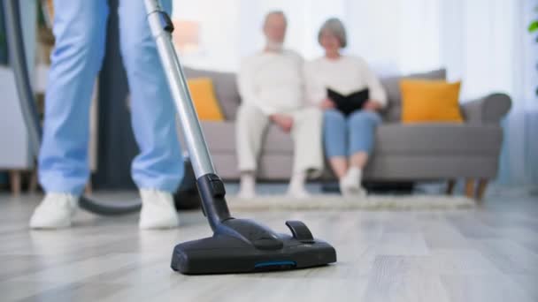 eläkeläisistä huolehtiminen, naispuolinen sosiaalityöntekijä pitää hauskaa siivotessaan vanhusten avioparin huonetta ja tanssien pölynimurilla käsissä, lähikuva - Materiaali, video