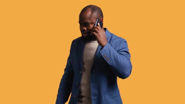 Joyous man with positive emotion, enjoying talking with friends in phone call using smartphone, studio background. Happy person with smile on face, receiving good news during telephone call, camera B - Footage, Video