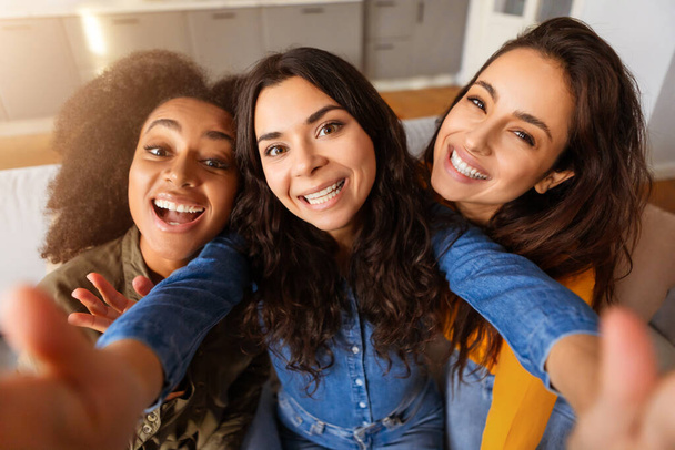 Fröhliche, multiethnische junge Frauen, die zu Hause einen Selfie-Moment festhalten, warme Freundschaft zeigen und lächeln - Foto, Bild