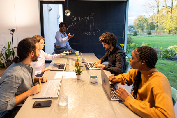 Esta foto captura un momento dinámico dentro de un equipo diverso que participa en una reunión de negocios. El entorno es un espacio de oficina contemporáneo bañado en luz natural, con una vista clara del verde al aire libre. A - Foto, Imagen