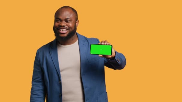 孤立したスクリーンフォンを持っている興奮したアフリカ系アメリカ人男性は,推奨事項を行います. モックアップスマートフォンを提示し,スタジオの背景,カメラAに隔離された肯定的なフィードバックを示すジョヨウスの人 - 映像、動画