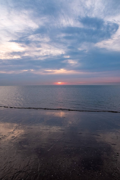 この写真は朝の静かな美しさを捉え,太陽が穏やかに海の地平線を照らしています. 雲の向こうの光と影の静かな遊び,そして柔らかい反射 - 写真・画像