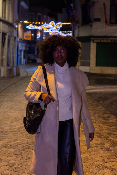 Tento portrét zachycuje ženu, jak jde na noční procházku městskou uličkou, ozdobenou blikajícími slavnostními světly. Jemné osvětlení okolí jemně zvýrazňuje její postavu a - Fotografie, Obrázek