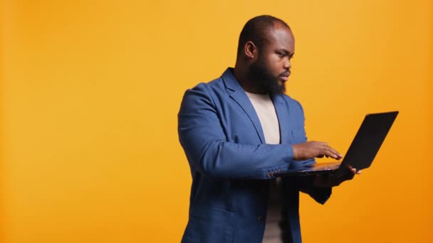 Homem afro-americano usando laptop para fazer tarefas relacionadas a negócios para a empresa, isolado sobre fundo de estúdio. Escritório fazendo orçamento, previsão e análise financeira no notebook, câmera B - Filmagem, Vídeo