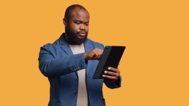 Man happily scrolling on tablet touchscreen to check social media feed. African american person browsing internet websites, entertained by content, studio background, camera A - Footage, Video