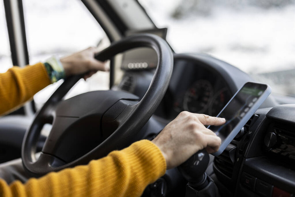 Руки водителя в ярком желтом свитере с помощью GPS планшета для навигации по заснеженной дороге. - Фото, изображение