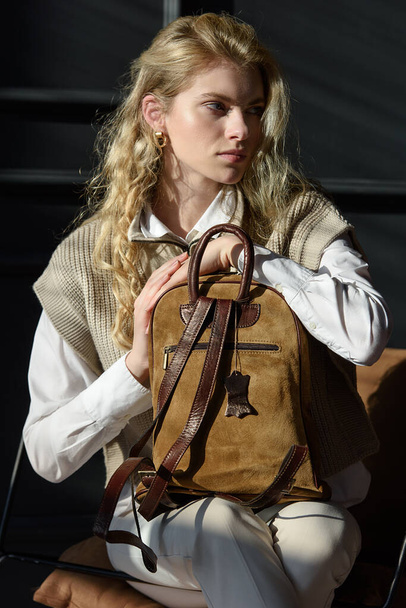 A woman holds leather backpack. Model wearing stylish knitted vest, white shirt and classic trousers. - Photo, Image