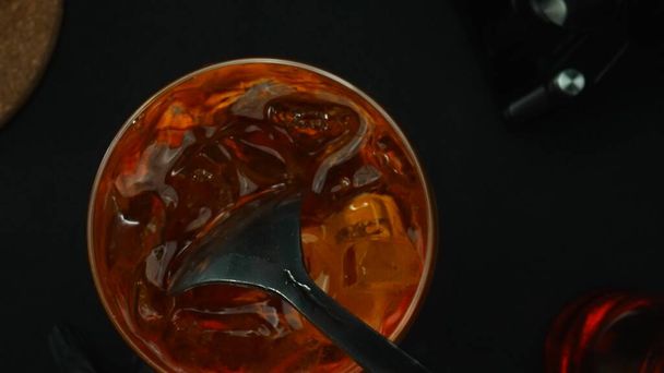 Macrographie, découvrez l'art de mélanger un cocktail Negroni dans une perspective descendante, orné d'une tranche d'orange fraîche et vibrante, le tout sur un fond noir dramatique. Vue de haut en bas. Comestible. - Photo, image