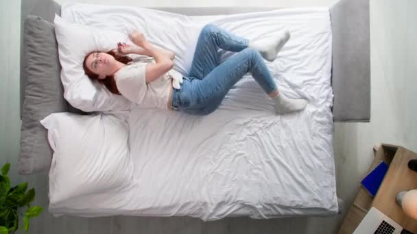 νεαρή γυναίκα προσπαθεί να χαλαρώσει λόγω νευρικού κλονισμού στο κρεβάτι στο υπνοδωμάτιο, top view - Πλάνα, βίντεο