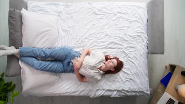 σκεπτική γυναίκα ξαπλώνει με τα πόδια στο μαξιλάρι ενώ ξεκουράζεται και σηκώνεται από το κρεβάτι, πάνω όψη - Πλάνα, βίντεο