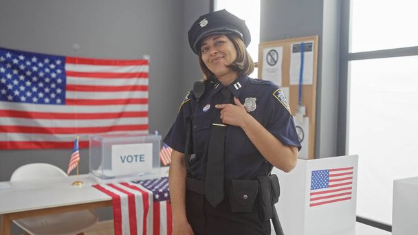 Una oficial confiada señalando su etiqueta de 'voté' en un centro de votación con banderas americanas. - Foto, imagen