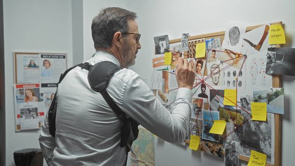 Un homme mûr analyse un tableau de preuves d'un crime dans le bureau d'un inspecteur, entouré de photos, de notes et d'empreintes digitales. - Photo, image
