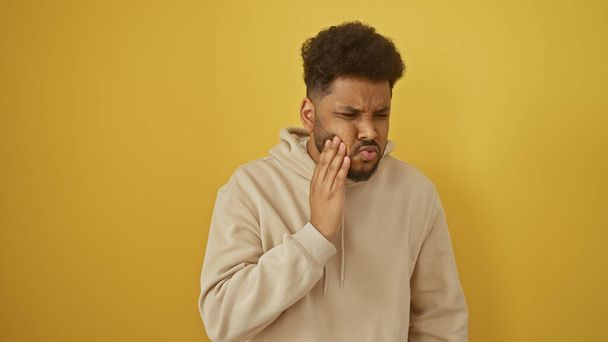 African american man with toothache isolated on yellow background, expressing pain and discomfort in casual attire. - Photo, Image
