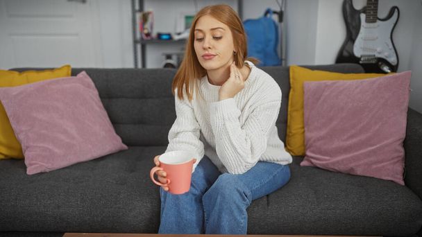 Entspannte junge Frau genießt einen gemütlichen Moment mit Kaffee auf einem bequemen Sofa zu Hause - Foto, Bild