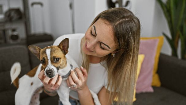 Una joven mujer rubia acaricia a su pequeño perro en el interior, mostrando compañía y cuidado en un ambiente acogedor en el hogar. - Foto, Imagen