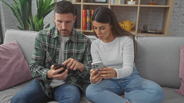Ein Mann und eine Frau konzentrieren sich auf ihre Smartphones, während sie zusammen auf einem Sofa in einem gemütlichen Wohnzimmer sitzen. - Foto, Bild