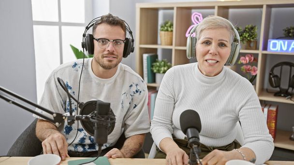 Mężczyzna i kobieta w słuchawkach mówiący do mikrofonów w jasnym studiu radiowym ze znakiem "na antenie" - Zdjęcie, obraz