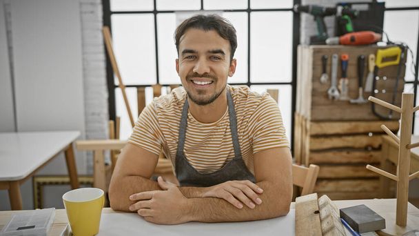 Glimlachende Spaanse man met baard in timmerwerkplaats omringd door gereedschap - Foto, afbeelding