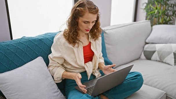 Összpontosított fiatal nő ül a nappaliban kanapé, szándékosan használ laptop technológia otthon. egy komoly portré egy gyönyörű, koncentrált kaukázusi felnőttről az eszközén, beltéri munkájába merülve.. - Fotó, kép