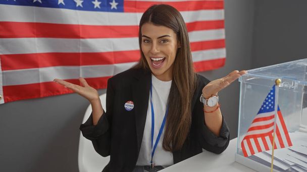 Mujer hispana sonriendo cerca de bandera americana en colegio electoral vistiendo etiqueta 'voté'. - Foto, imagen