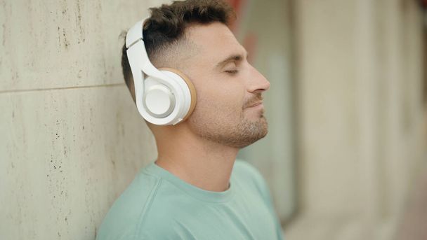 Young hispanic man listening to music standing at street - Photo, image