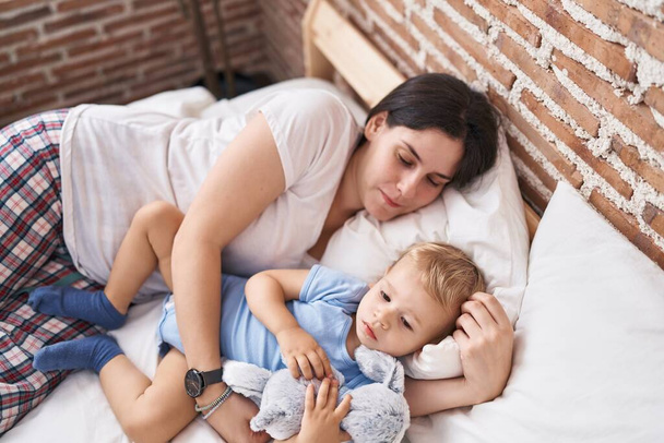 Μητέρα και γιος ξαπλωμένοι στο κρεβάτι αγκαλιάζοντας κούκλα στο υπνοδωμάτιο - Φωτογραφία, εικόνα