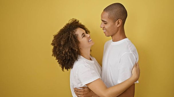 Confident beautiful couple, sharing a joyful yellow background hug, smiling in their isolated wonderland of love, happiness radiating from their casual stance. - Photo, Image