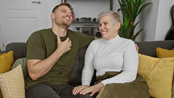 Смеющиеся зрелая женщина и молодой человек, сидящие вместе на диване в уютной гостиной - Фото, изображение