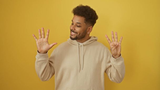 Glimlachende zwarte man maakt nummer negen gebaar tegen gele achtergrond - Foto, afbeelding