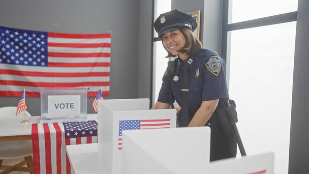 Una oficial de policía sonriente supervisando una estación de votación con cabinas, banderas americanas y una urna en el interior. - Foto, imagen