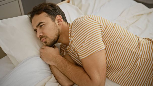 Красивий молодий іспаномовний чоловік з бородою, що лежить задумливо в спальні. - Фото, зображення