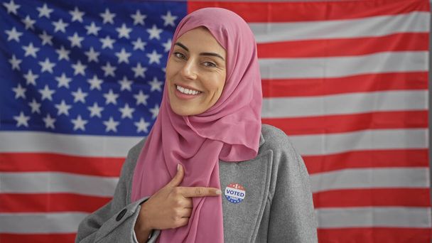 Uśmiechnięta kobieta w hidżabie z naklejką "Głosowałem", amerykańska flaga, reprezentująca różnorodność i demokrację. - Zdjęcie, obraz