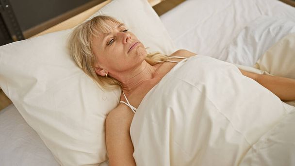 Занепокоєна біла жінка середнього віку лежить в ліжку у своїй спальні, дивлячись споглядально і, можливо, погано. - Фото, зображення
