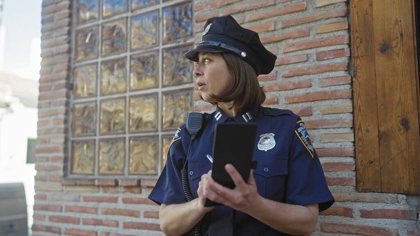 Widok z boku skupionej policjantki robiącej notatki na notatniku pod ścianą z cegły. - Zdjęcie, obraz