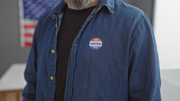 Primo piano di un uomo barbuto che indossa un adesivo 'votato' con una bandiera americana sullo sfondo che simboleggia la democrazia degli Stati Uniti. - Foto, immagini