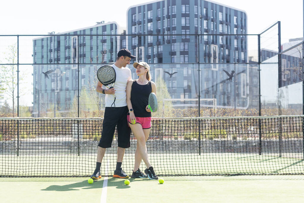 Sportovní pár s padelovými raketami pózující na tenisovém kurtu. Kvalitní fotografie - Fotografie, Obrázek